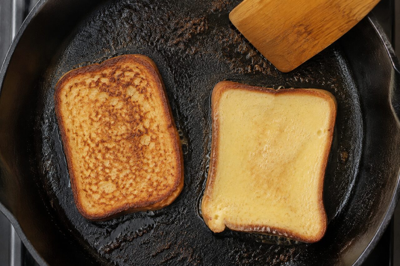 Two slices in a black skillet, one an even mid bronze with a fine crackled surface and one still pale yellow with only a faint tan haze